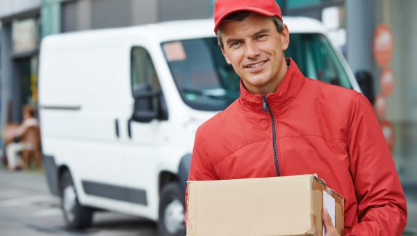 Smiling male postal delivery courier man outdoors  in front of cargo van delivering package